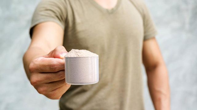 Man holding a whey protein on gray background. - a man holding a cup of protein powder