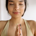 - A peaceful woman meditating with closed eyes in a yoga pose, embracing mindfulness indoors.