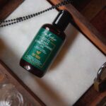 10 Best Beard Oils for Seborrheic Dermatitis in 2023: Our Top Picks - Beard conditioning oil bottle on a rustic wooden tray with a lock and chain, top view.