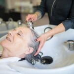 Best 5 Hair Dyes for Seborrheic Dermatitis - Top Choices for 2023 - Elderly woman enjoying a soothing hair wash in a stylish Portuguese salon, capturing a tranquil moment.