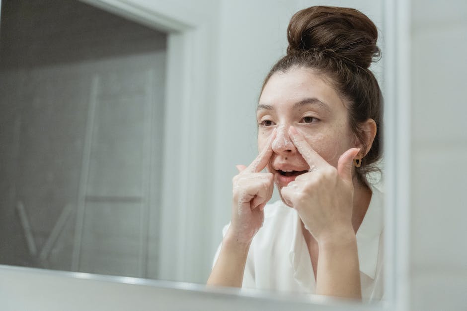 Best Seborrheic Dermatitis Face Washes 2026 | SebDermatology - A young woman applies skincare in front of a bathroom mirror, focusing on facial care.