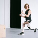Complete Summer Seb Derm Survival Guide: Heat, Sweat & Humidity Management - A young woman performing lunges with dumbbells in a modern indoor gym setting.