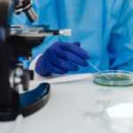 Gut Microbiome and Seborrheic Dermatitis: How Digestive Health May Affect Your Skin (2026) - Scientist in laboratory examining samples using a microscope and Petri dish, wearing protective gloves.