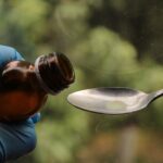 Luliconazole Shampoo for Seborrheic Dermatitis: What Research Shows (2026) - Close-up of syrup being poured from a bottle into a spoon by gloved hands, medical concept.