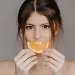 Malassezia-Safe Diet for Seborrheic Dermatitis: Which Foods Actually Matter - Close-up portrait of a woman holding a half orange slice, with a focus on natural beauty and skincare.