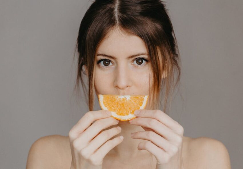 Malassezia-Safe Diet for Seborrheic Dermatitis: Which Foods Actually Matter - Close-up portrait of a woman holding a half orange slice, with a focus on natural beauty and skincare.