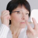 Managing Seborrheic Dermatitis with Head and Shoulders: Proven Effectiveness and Expert Insights - A senior woman in a cozy sweater applying mascara with a focused expression indoors.