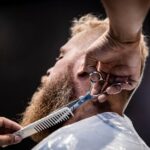 MCT Oil for Seborrheic Dermatitis: Why Malassezia-Safe Moisturizing Works (2026) - Close-up of a barber trimming a client's beard with scissors and comb.