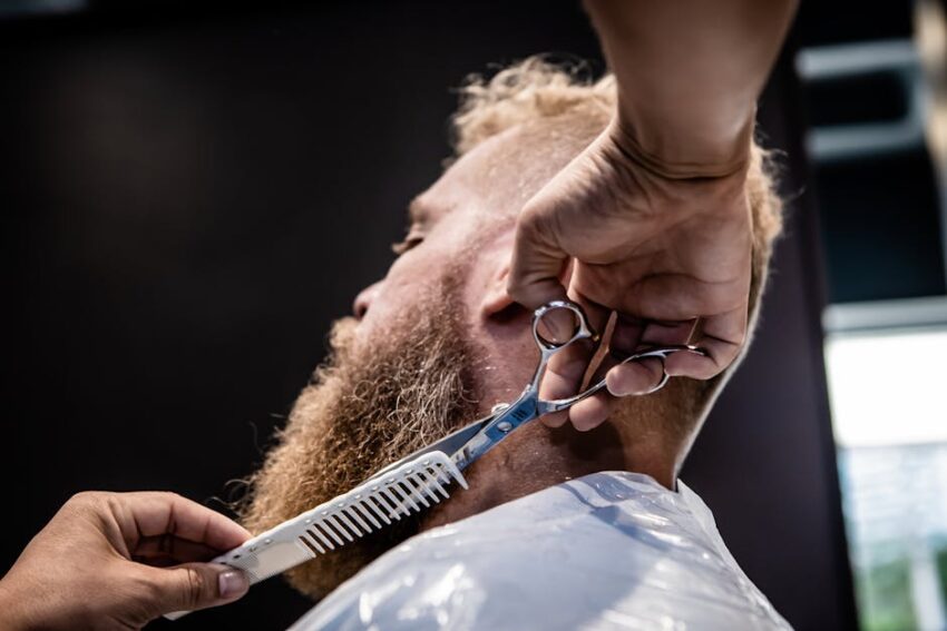 MCT Oil for Seborrheic Dermatitis: Why Malassezia-Safe Moisturizing Works (2026) 1 MCT Oil for Seborrheic Dermatitis: Why Malassezia-Safe Moisturizing Works (2026) - Close-up of a barber trimming a client's beard with scissors and comb.