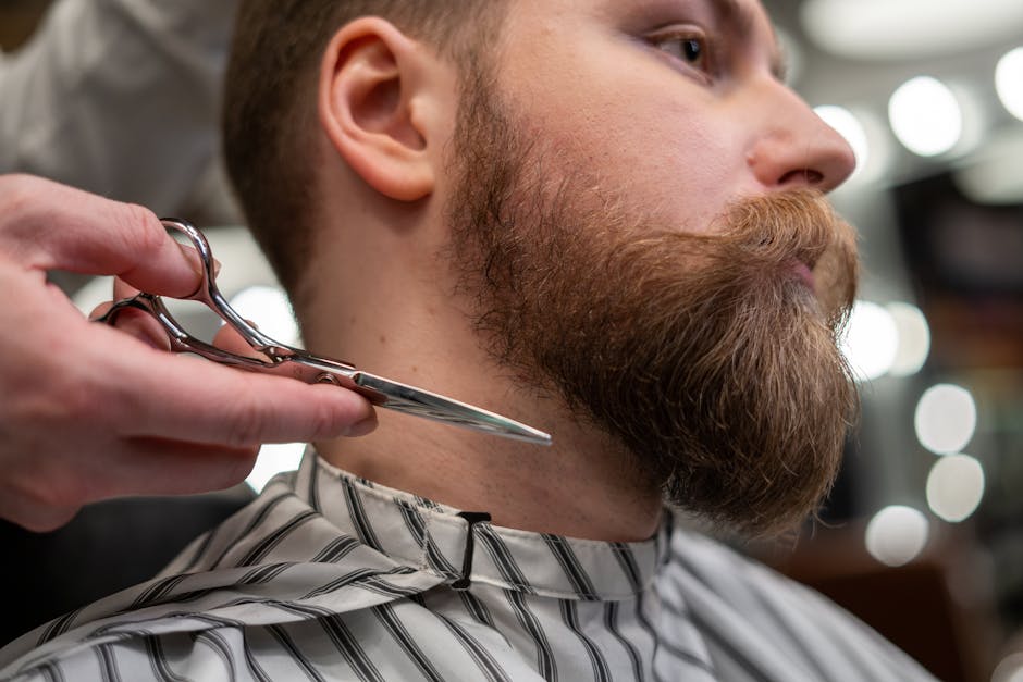 Seborrheic Dermatitis Beard Care: How to Treat Beard Dandruff Without Ruining Your Facial Hair (2026) 7 Seborrheic Dermatitis Beard Care: How to Treat Beard Dandruff Without Ruining Your Facial Hair (2026) - Detailed shot of a barber trimming a man's beard with scissors in a barbershop.