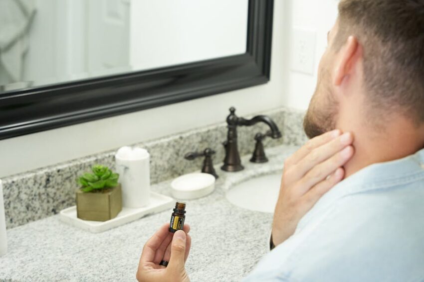 Seborrheic Dermatitis Beard Treatment Guide 2026: How to Manage Flaking, Itching & Redness Under Facial Hair - Adult man in bathroom holding an essential oil bottle near mirror, focusing on grooming and self-care.