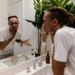 Seborrheic Dermatitis vs Dry Skin on the Face: How to Tell the Difference - A young man applying skincare product while looking in the mirror in a modern bathroom.
