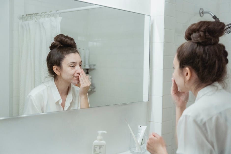Seborrheic Dermatitis vs Dry Skin on the Face: How to Tell the Difference - Caucasian woman in bathroom applying skincare product while looking in the mirror.