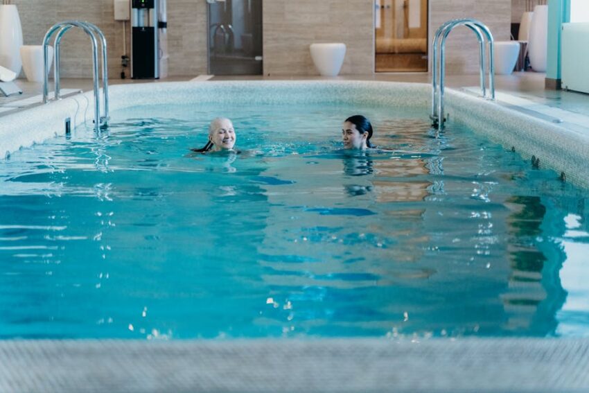 Swimming & Seb Derm: 2026 Safety Guide | SebDermatology - Senior woman and adult woman enjoying a relaxing swim in an indoor pool, featuring leisure and relaxation.