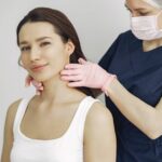 The pH Connection: How Balancing Your Skin's pH Can Help Treat Seborrheic Dermatitis - A medical practitioner in scrub suit performs a neck examination on a smiling woman in a clinic.