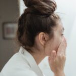 The Ultimate Guide to Treating Seborrheic Dermatitis: Find Your Perfect Face Wash - A young woman in a bathrobe follows her skincare routine, washing her face in a bathroom.
