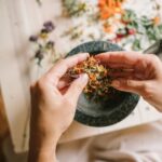 Unveiling Effective Cultural Remedies for Seborrheic Dermatitis - Close-up of hands preparing herbal ingredients in a mortar and pestle, top view.