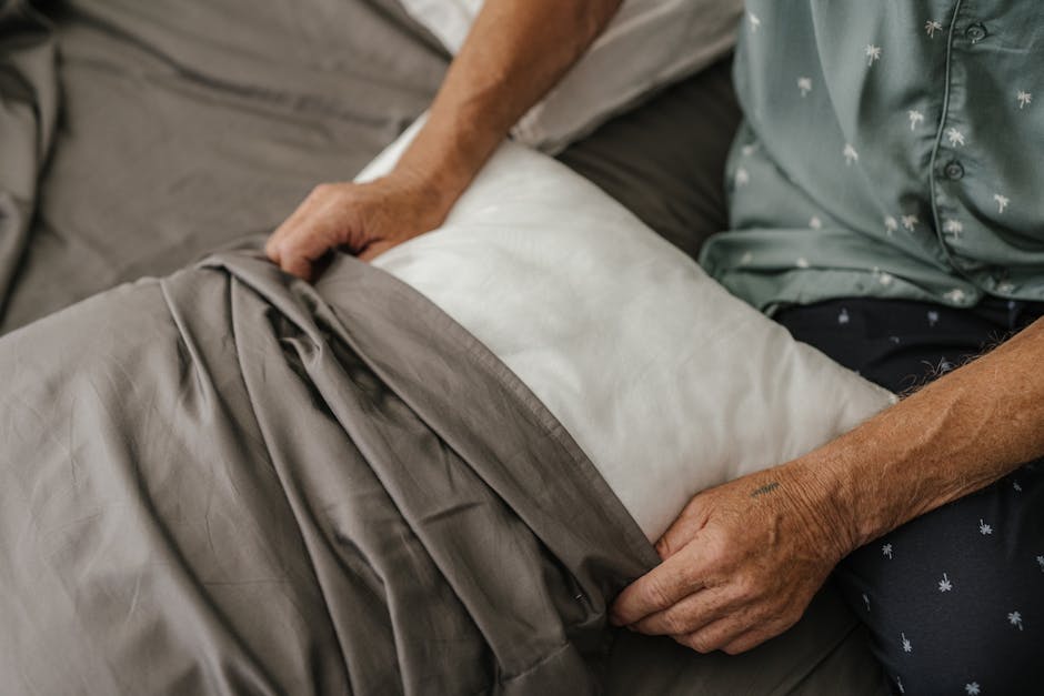 Upgrade Your Sleep Routine: The Best Cotton Pillowcases for Seborrheic Dermatitis - Close-up of a senior adult carefully arranging a bed with grey sheets and a white pillow.