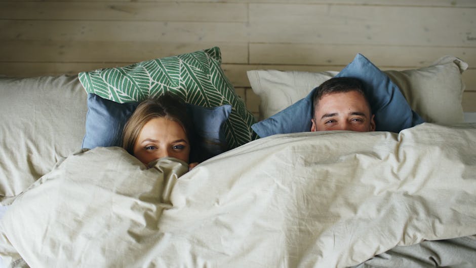 Upgrade Your Sleep Routine: The Best Cotton Pillowcases for Seborrheic Dermatitis - A man and woman snuggled under blankets in a cozy, pillow-filled bed.