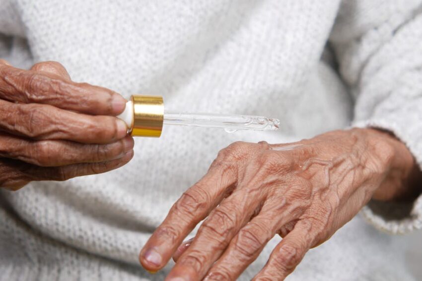 Winning Title: Can Helping Your Immune System Aid In Managing Seborrheic Dermatitis? - Close-up of elderly hands applying serum with dropper, focusing on skincare and aging.