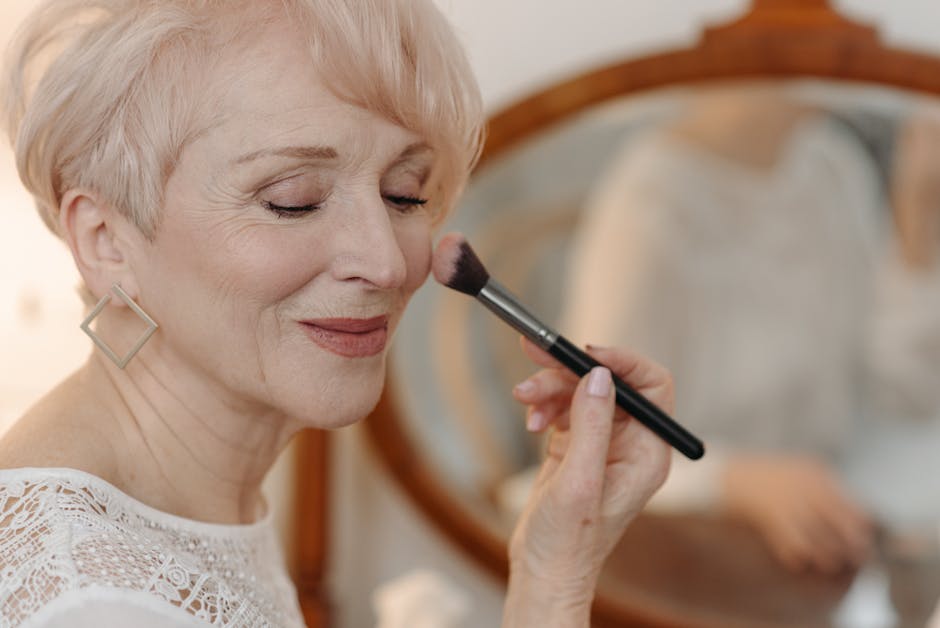 Winning Title: Can Helping Your Immune System Aid In Managing Seborrheic Dermatitis? - Close-up of a senior woman applying makeup while smiling gracefully indoors.