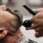 safe-face-oils-seborrheic-dermatitis-2026 - Close-up of a barber using clippers to groom a client's beard in a barbershop.