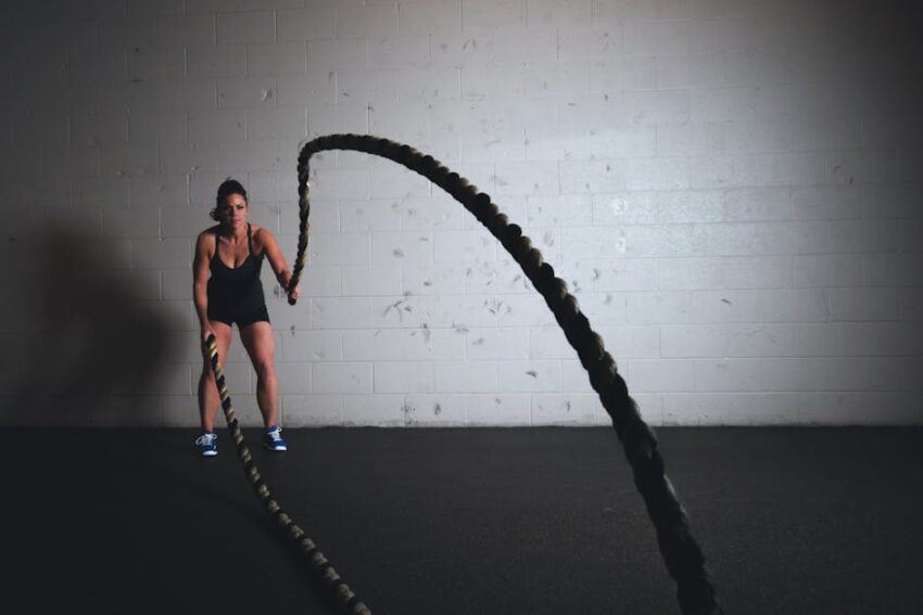 sweat-wicking-products-seborrheic-dermatitis-summer-2026 - A focused woman performs a dynamic battle rope exercise in a gym setting, demonstrating strength and fitness.