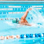 Swimming & Seb Derm: 2026 Safety Guide | SebDermatology - Energetic swimmer performing a stroke in a bright outdoor pool under sunlight in Maceió, Brazil.