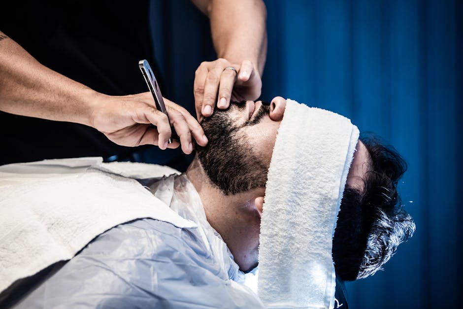 tea-tree-oil-seborrheic-dermatitis-guide-2026 - An adult man receiving a precise beard trim in a barbershop with a warm towel treatment.